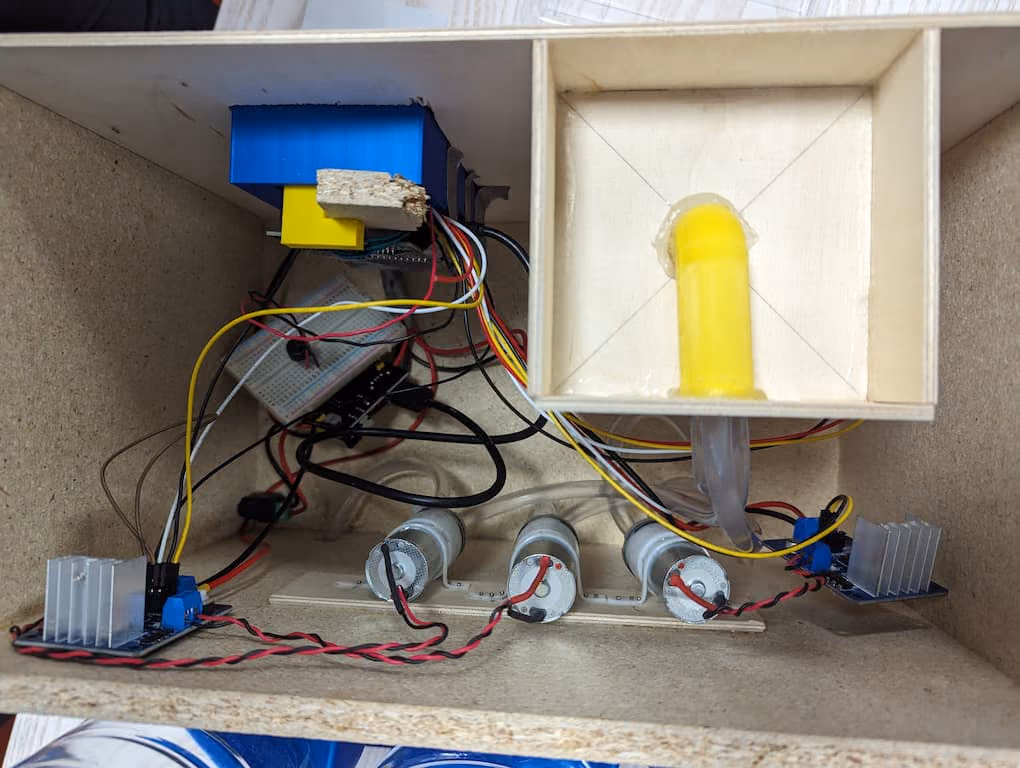 Inside the case: three diaphragm pumps in a row, two power modules with heat sinks, a breadboard with the Pico, and a 3D printed yellow tube guide leading into the dispensing bay